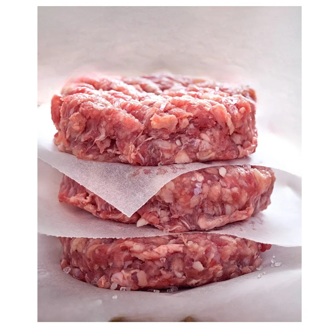 Three raw ground meat patties stacked on a white surface with wax paper underneath.